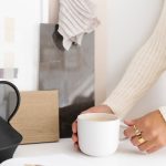 woman holding a cup of coffee that is sitting on a white counter