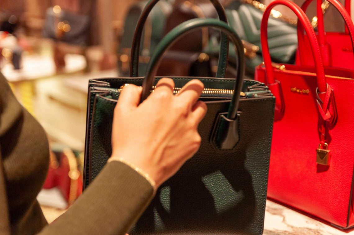 a lady's hand holding a black back in a department store with lots of handbags