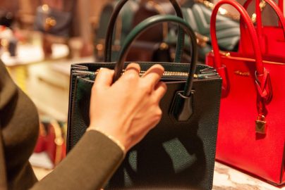 a lady's hand holding a black back in a department store with lots of handbags
