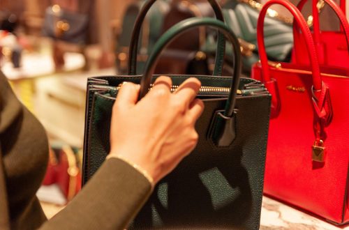 a lady's hand holding a black back in a department store with lots of handbags