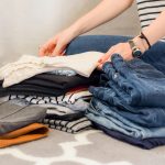Woman organizing a travel wardrobe with folded jeans and neutral outfits for packing.