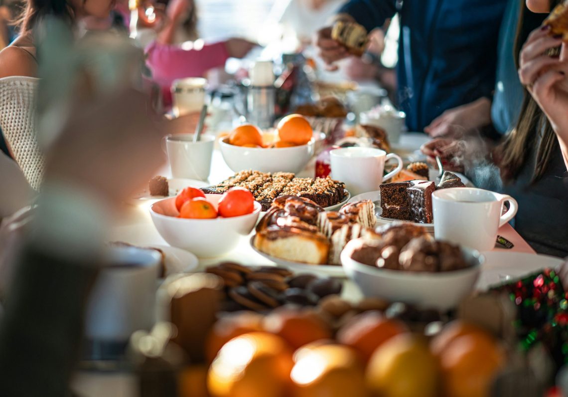People gathered around a table filled with pastries, fruit, desserts, and coffee during a cozy brunch.