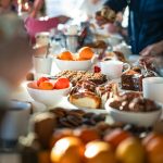 People gathered around a table filled with pastries, fruit, desserts, and coffee during a cozy brunch.