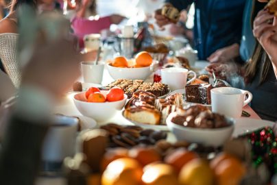 People gathered around a table filled with pastries, fruit, desserts, and coffee during a cozy brunch.