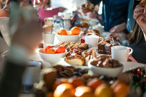People gathered around a table filled with pastries, fruit, desserts, and coffee during a cozy brunch.