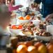 People gathered around a table filled with pastries, fruit, desserts, and coffee during a cozy brunch.