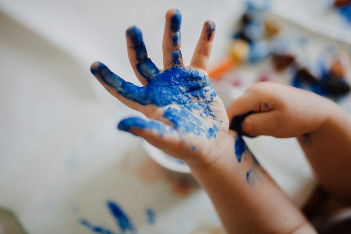 Close-up of a child’s hands covered in bright blue paint during a messy arts and crafts activity indoors.