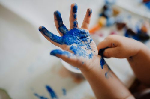 Close-up of a child’s hands covered in bright blue paint during a messy arts and crafts activity indoors.