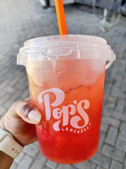 My hand holding a bucket of strawberry watermelon Pop's Lemonade.