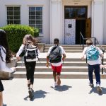 Children wearing backpacks run toward the entrance of a school on the first day of class, representing the transition to a new school year and middle school.