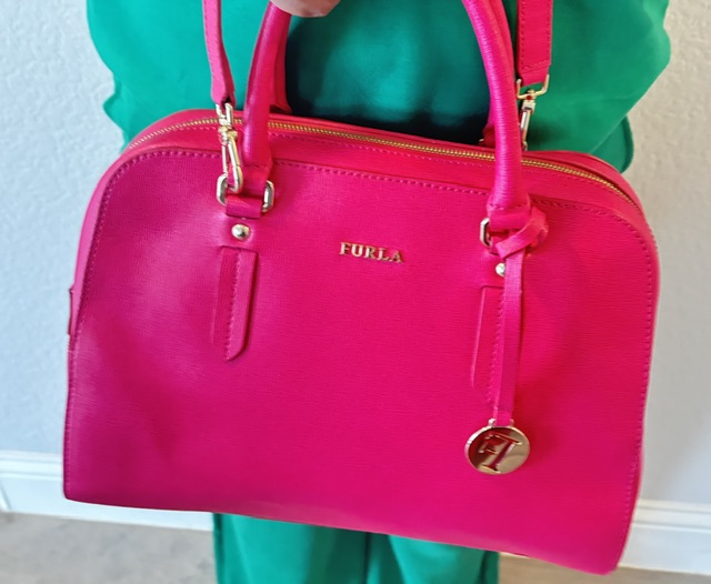 Bright pink Furla leather satchel handbag styled with a green outfit, featuring gold hardware and a structured design.